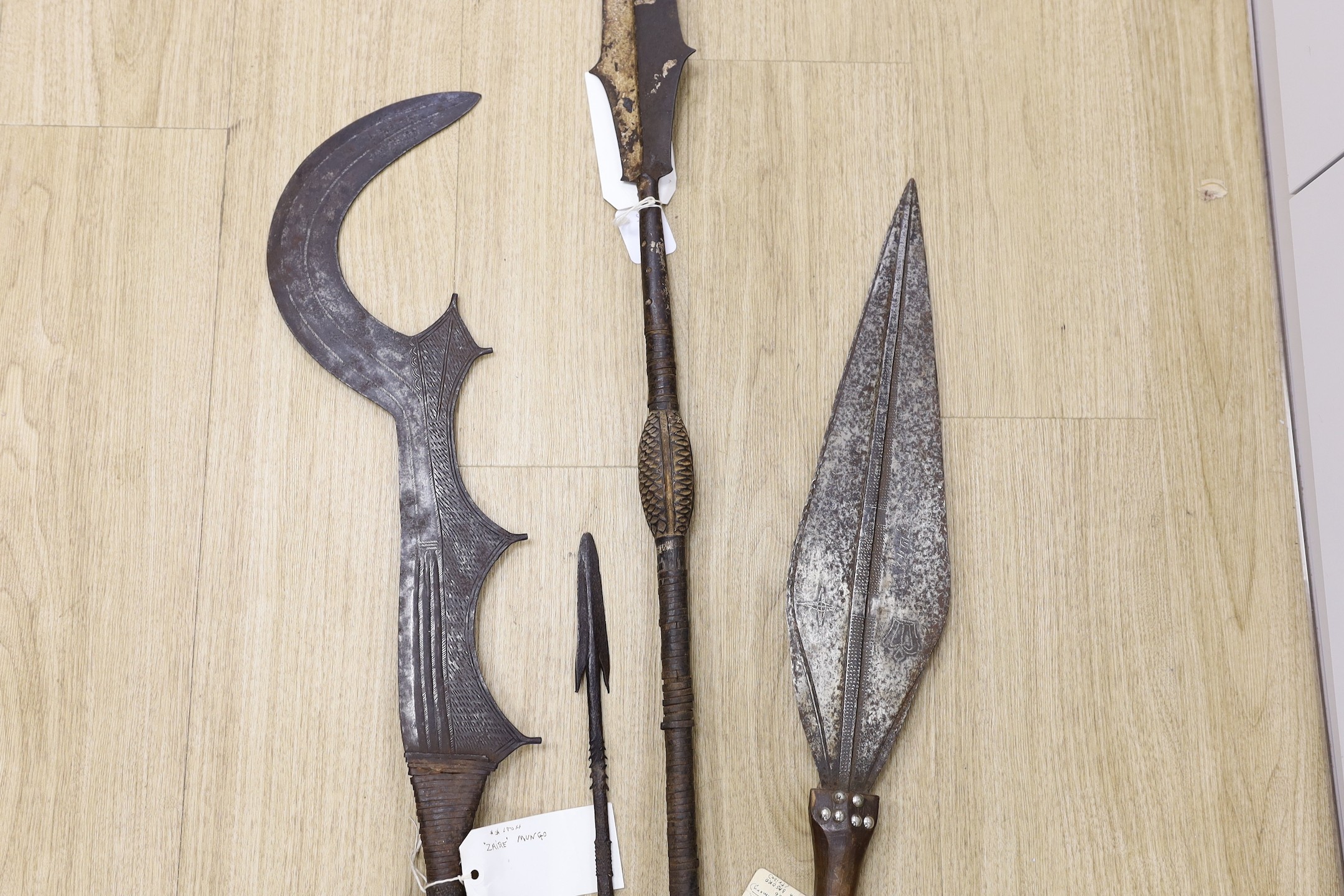 A group of African tribal weapons including an Ngombe ceremonial sword, a similar spear, Democratic Republic of Congo, a Kuba sword and a spear head, spear length 148.5cm